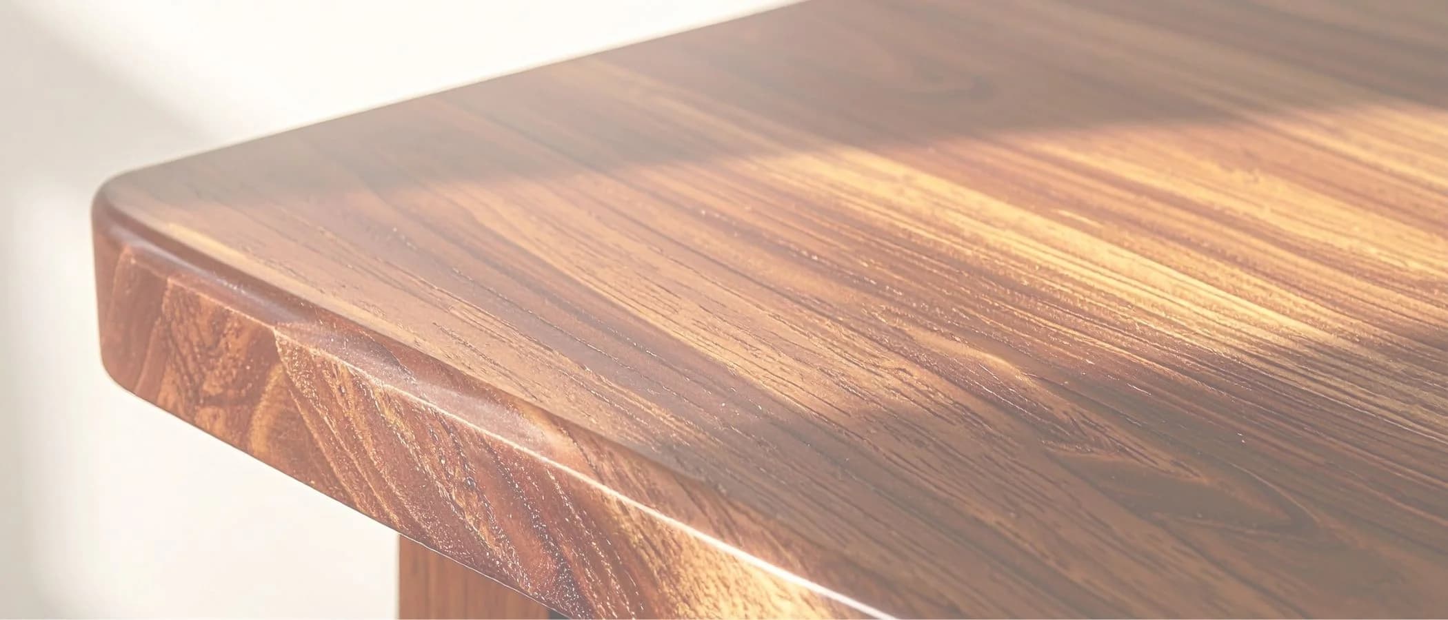 Close-up of a beautifully finished solid dark wood tabletop corner with soft sunlight highlights