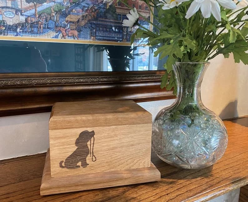 Handcrafted white oak pet memorial urn with laser-engraved silhouette of a sitting dog holding a leash in its mouth